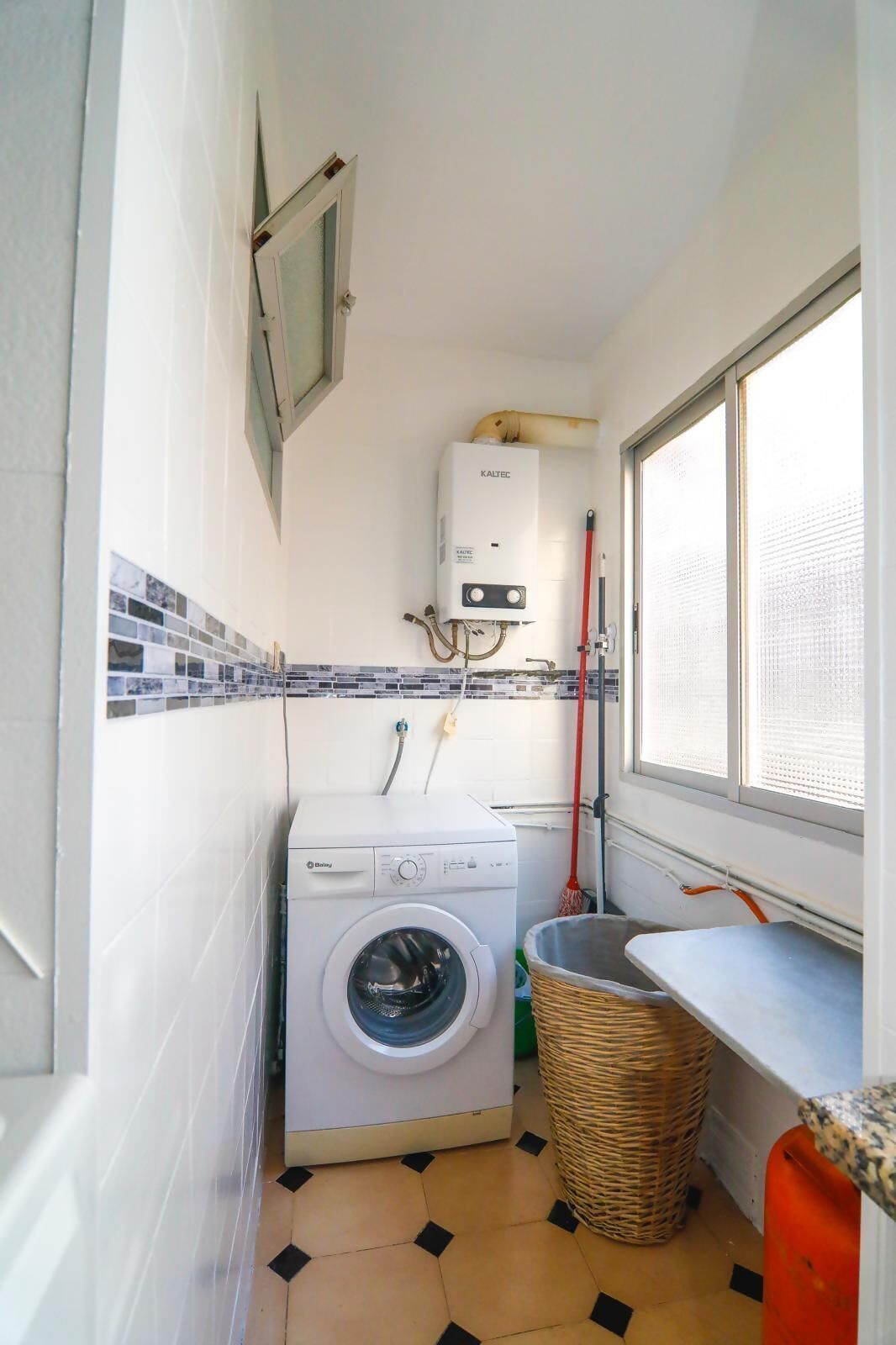 Une petite buanderie équipée d’un lave-linge, d’un radiateur et d’une fenêtre.