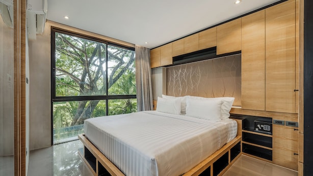 Ein modernes Schlafzimmer mit einem großen Bett, eingebauten Holzschränken und Blick auf Grün hinter einem großen Fenster.