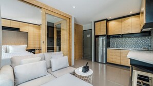 Ein modernes Wohnzimmer mit einer Couch, einem kleinen runden Tisch und einer Küchenzeile mit Holzschränken und einem Kühlschrank.