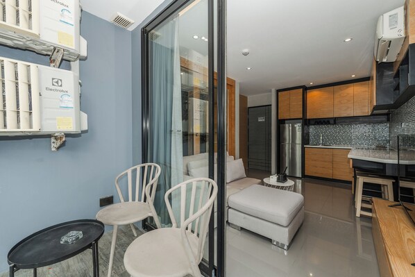 A modern living room with a glass partition, white furniture, and a kitchen area with wooden cabinets and a tiled backsplash.