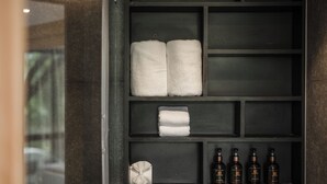 Ein Badezimmer mit dunkel gefliester Wand, Ablagefläche mit Handtüchern, Taschentuchbox und Toilettenartikeln.