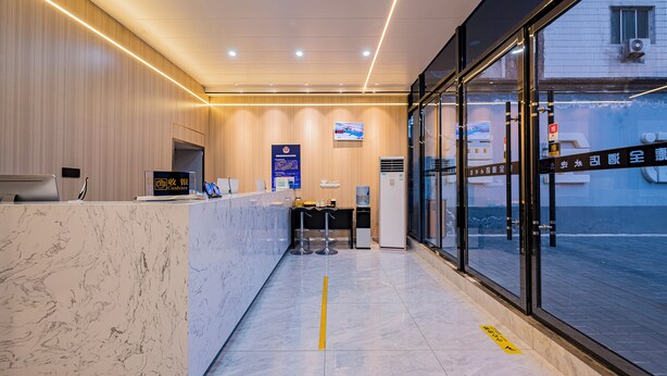 A modern hotel reception area with a marble counter, a TV mounted on the wall, and a glass door leading outside.