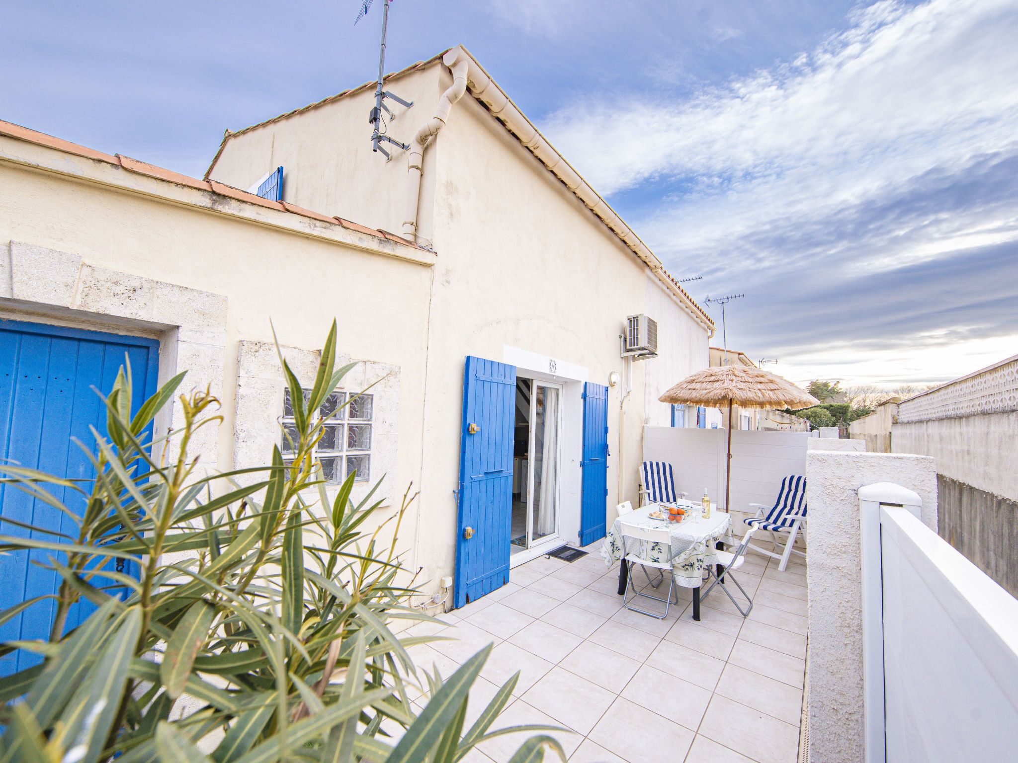 A patio with a table and chairs, a blue door, and a thatched umbrella.