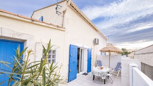 Une terrasse avec une table et des chaises, une porte bleue et un parasol en chaume.