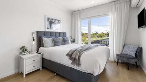 Une chambre à coucher avec un lit, une table de chevet, une chaise et une grande fenêtre avec des rideaux.