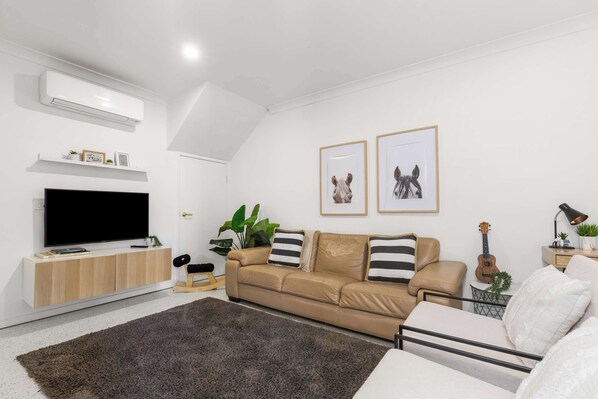 Un salon moderne avec un téléviseur à écran plat, un canapé beige, un tapis foncé et des tableaux encadrés accrochés au mur.