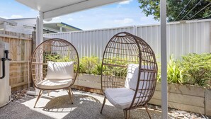 Deux chaises en osier avec des coussins, placées sous une terrasse couverte.