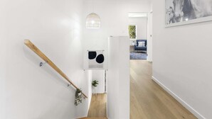 Un intérieur moderne avec un escalier en bois, des murs blancs et un luminaire suspendu.
