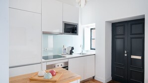 Une cuisine moderne avec des meubles blancs, un micro-ondes noir, un évier en acier inoxydable et un plan de travail en bois.