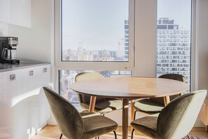 Enjoy a panoramic city view from the large window, with a dining area and kitchenette nearby.