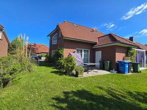 Een twee verdiepingen tellend bakstenen huis met een pannendak, een kleine tuin en een patio met een tafel en stoelen.