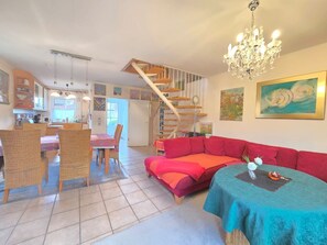 Een ruime woonkamer met een rode bank, een blauwgroene tafel en een spiltrap.
