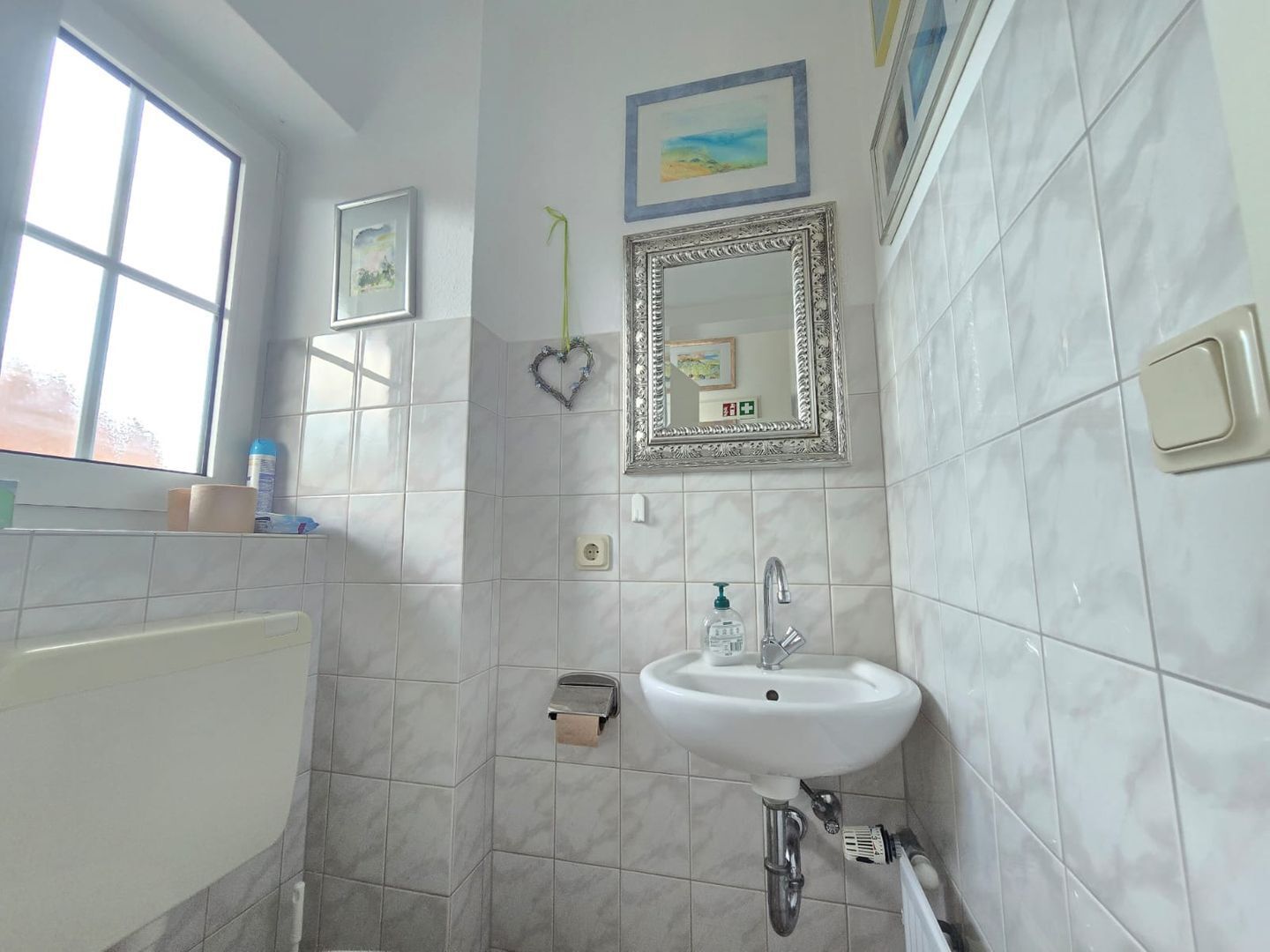 Une salle de bain avec un lavabo blanc, un miroir et une fenêtre.