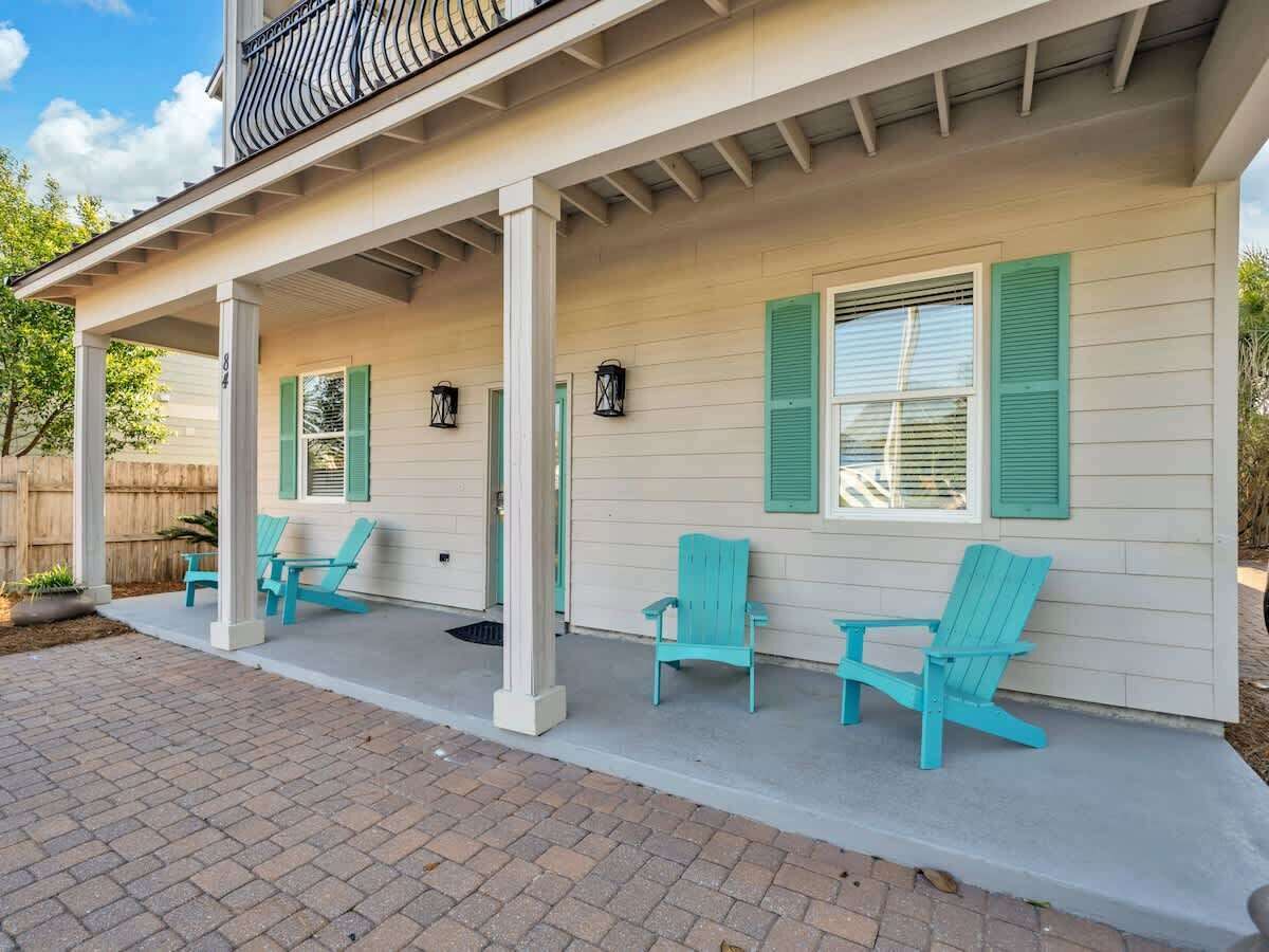 Une véranda couverte avec quatre fauteuils Adirondack turquoise et un chemin de briques menant à l’entrée.
