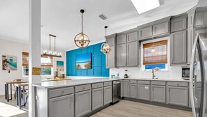 Une cuisine moderne avec des meubles gris, un mur d’accent bleu et un plancher en bois.
