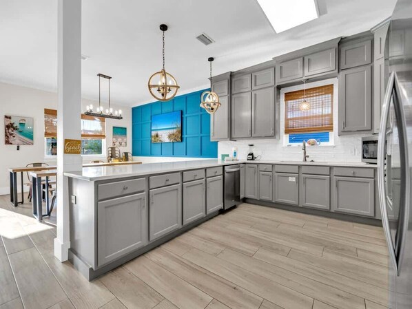 A modern kitchen with grey cabinets, a blue accent wall, and a wooden floor.