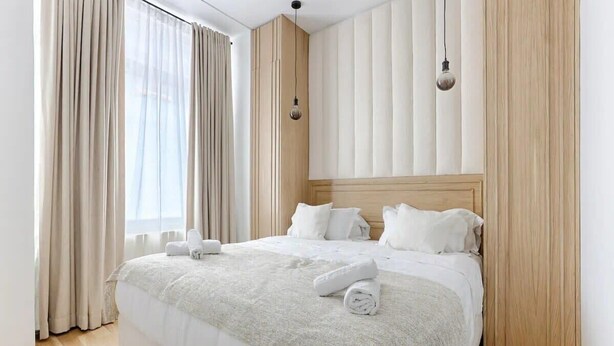 A hotel room with a large bed, beige curtains, and a wooden headboard.