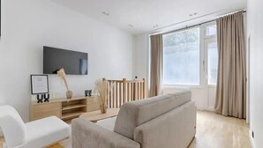 A modern living room with a flat-screen TV, a sofa, a chair, and a wooden table.