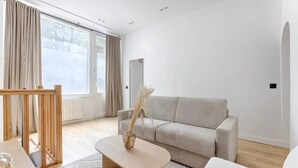 A modern living room with a grey sofa, a wooden coffee table with a vase, and a large window with curtains.