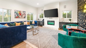 A modern living room with a large flat-screen TV, a sofa set, a coffee table, and a patterned rug.
