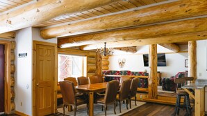 A wooden dining table with chairs, a chandelier, and a stone fireplace in a log cabin interior. - Silverthorne Retreat | Pet Friendly + Trail Access (Silverthorne)