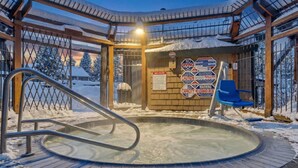 A hot tub with a metal ladder, surrounded by snow-covered ground and a wooden structure with warning signs. - Lake Tahoe Getaway – Close to Beach & Ski Slopes! (Tahoe City)