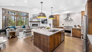 Una cocina moderna con una isla central, armarios de madera, electrodomésticos de acero inoxidable y un amplio ventanal con vistas a un bosque.