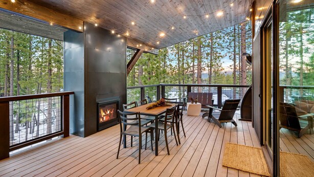 Terraza de madera con chimenea, asientos al aire libre y vista a árboles.