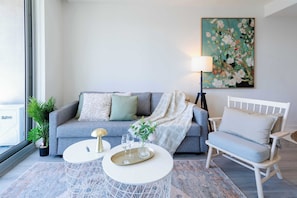 A modern living room with a grey sofa, a white armchair, a round coffee table, a floor lamp, and a large floral painting on the wall.