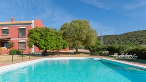 A swimming pool with lounge chairs, a red building, and a large tree. - Mazuecos Rural House  - Beautiful 3 bedroom finca in Sevilla (Lora del Río)