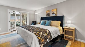 Un dormitorio con cama, mesita de noche, lámpara y vistas al exterior.