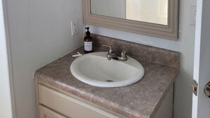 Un baño con lavamanos, espejo, aros para toallas y una botella de jabón para manos.