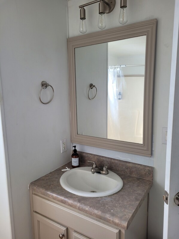 Un baño con lavamanos, espejo, aros para toallas y una botella de jabón para manos.