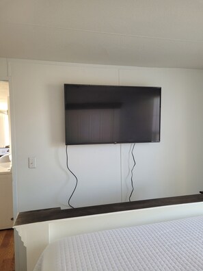 Un dormitorio con una televisión de pantalla plana montada en la pared, una cama con colchón blanco y un cabecero de madera oscura.