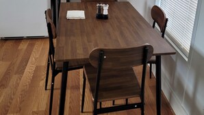 Un comedor con una mesa de madera, cuatro sillas y un ventanal con persianas.
