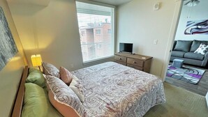 A bedroom with a bed, a dresser, a TV, and a window with blinds.