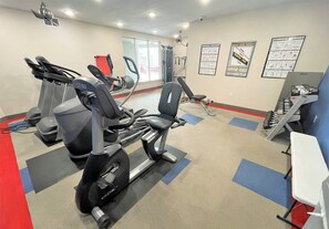 A gym with treadmills, a stationary bike, and a weight bench. There are posters on the wall and a white table with weights. - Luxury Condo in the Library Square District (Salt Lake City)