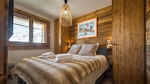 A bedroom with a large bed, wooden walls, a framed poster, and a window.
