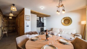 A dining area with a round wooden table set for four, a bottle of champagne, and a cozy seating arrangement with a fur throw.