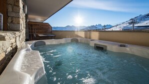 A hot tub with a mountainous view, stone walls, and a clear sky.