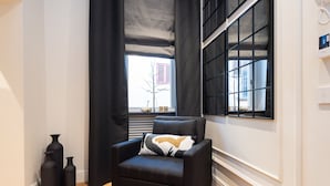 A modern living room with a black armchair, a window with black blinds, and decorative vases on the floor.