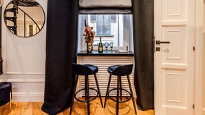 A modern kitchen with a window, two bar stools, a mirror, and a black curtain.