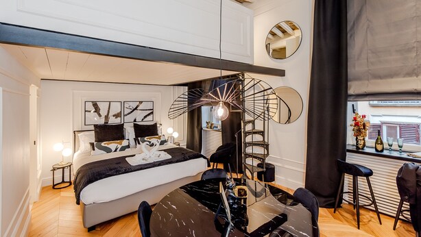 A modern bedroom with a large bed, a dining table, and a unique ceiling light fixture.