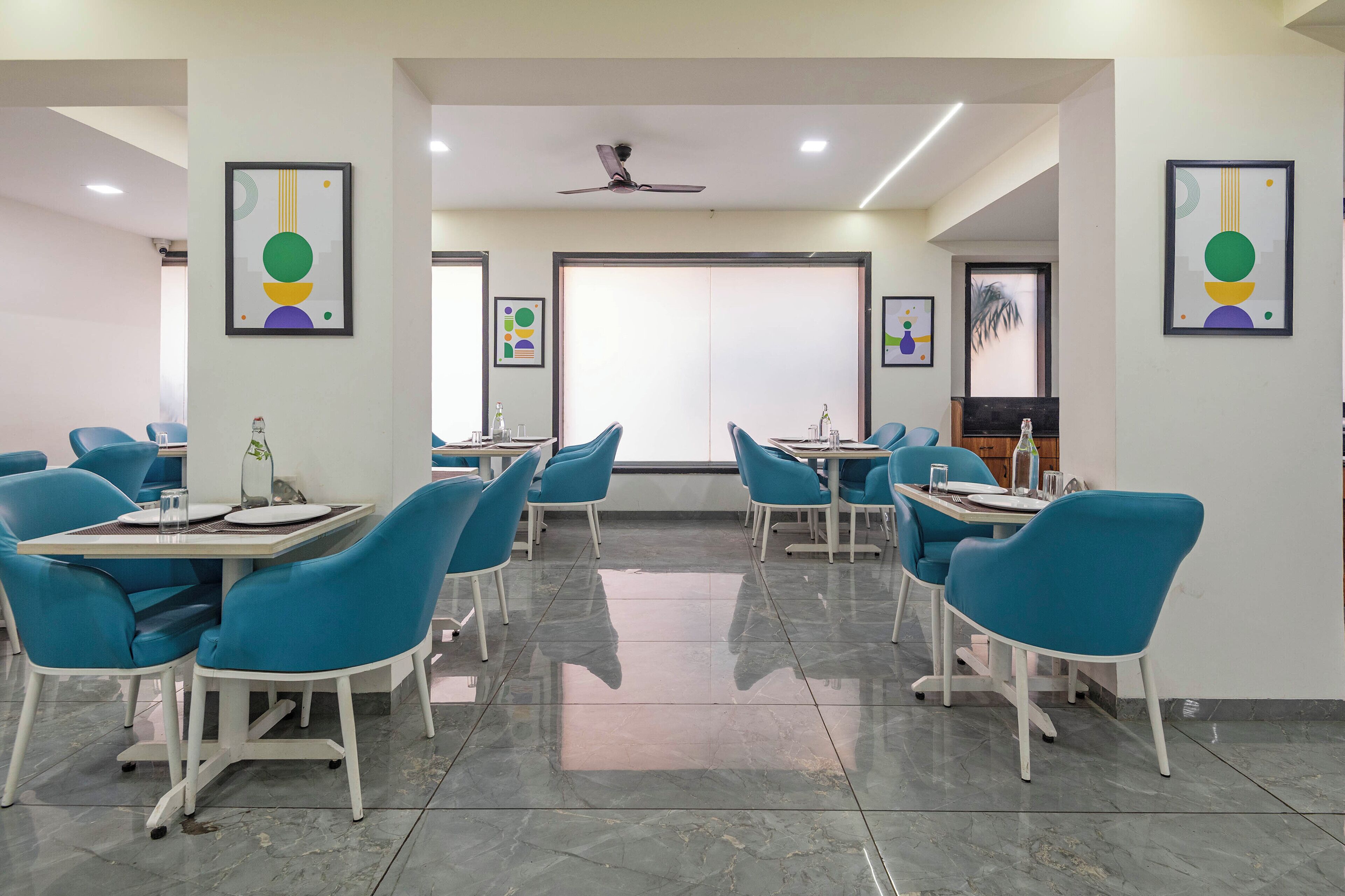 A modern conference room with blue chairs and tables, a ceiling fan, and abstract art on the walls.