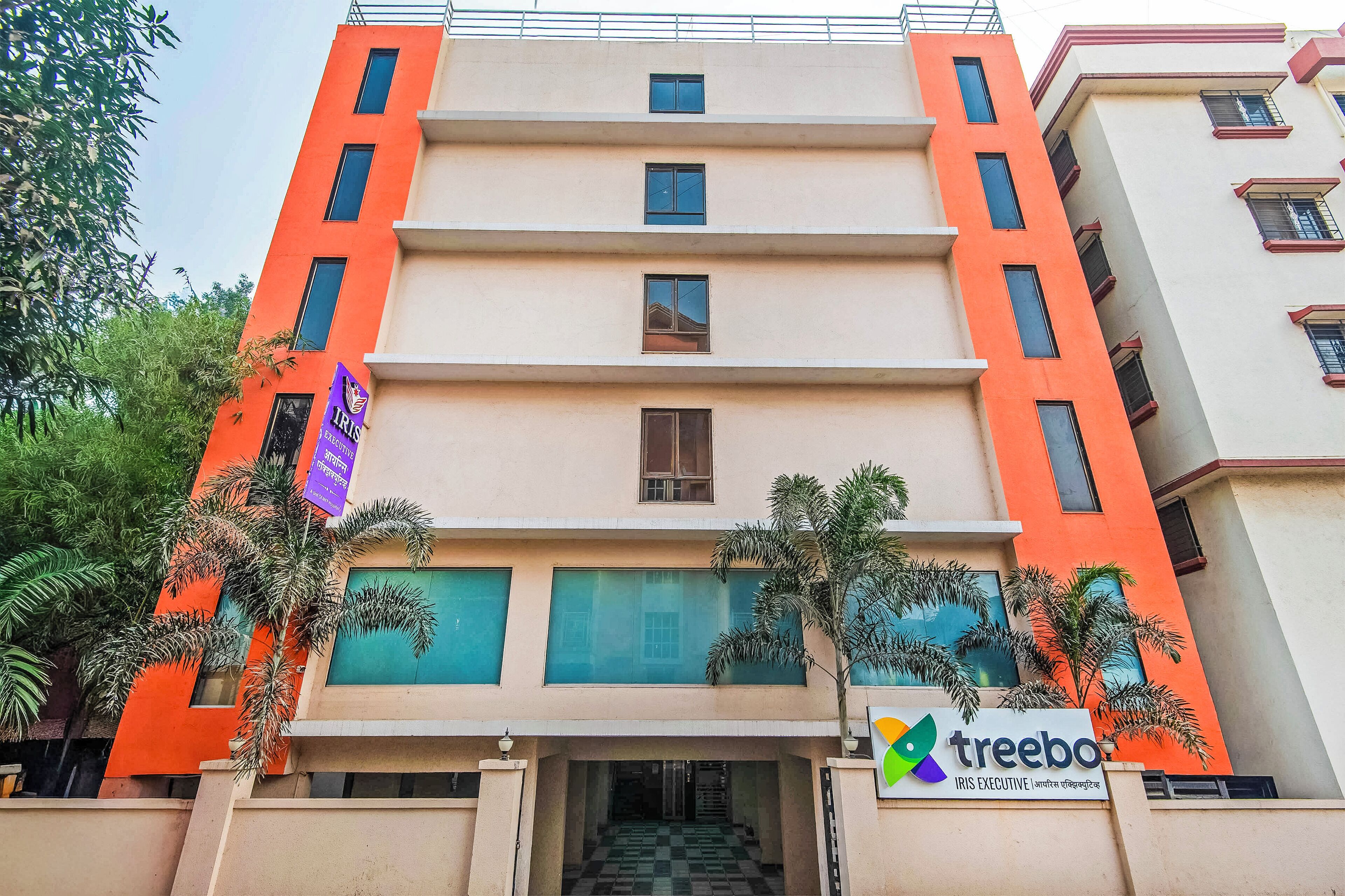 A multi-story building with a prominent orange facade, a visible entrance with a checkered floor, and a sign for 'treebo' at the bottom.