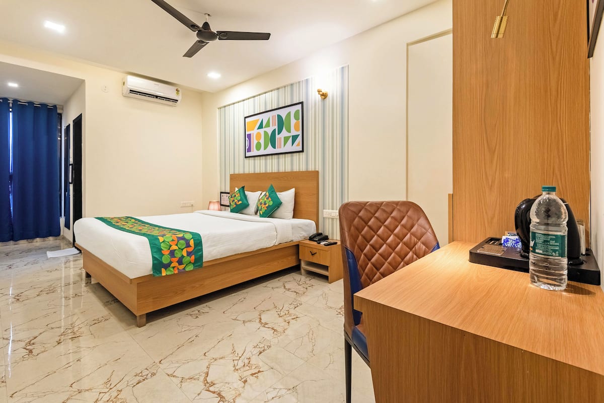 A hotel room with a bed, a desk, a chair, a ceiling fan, and an air conditioning unit.