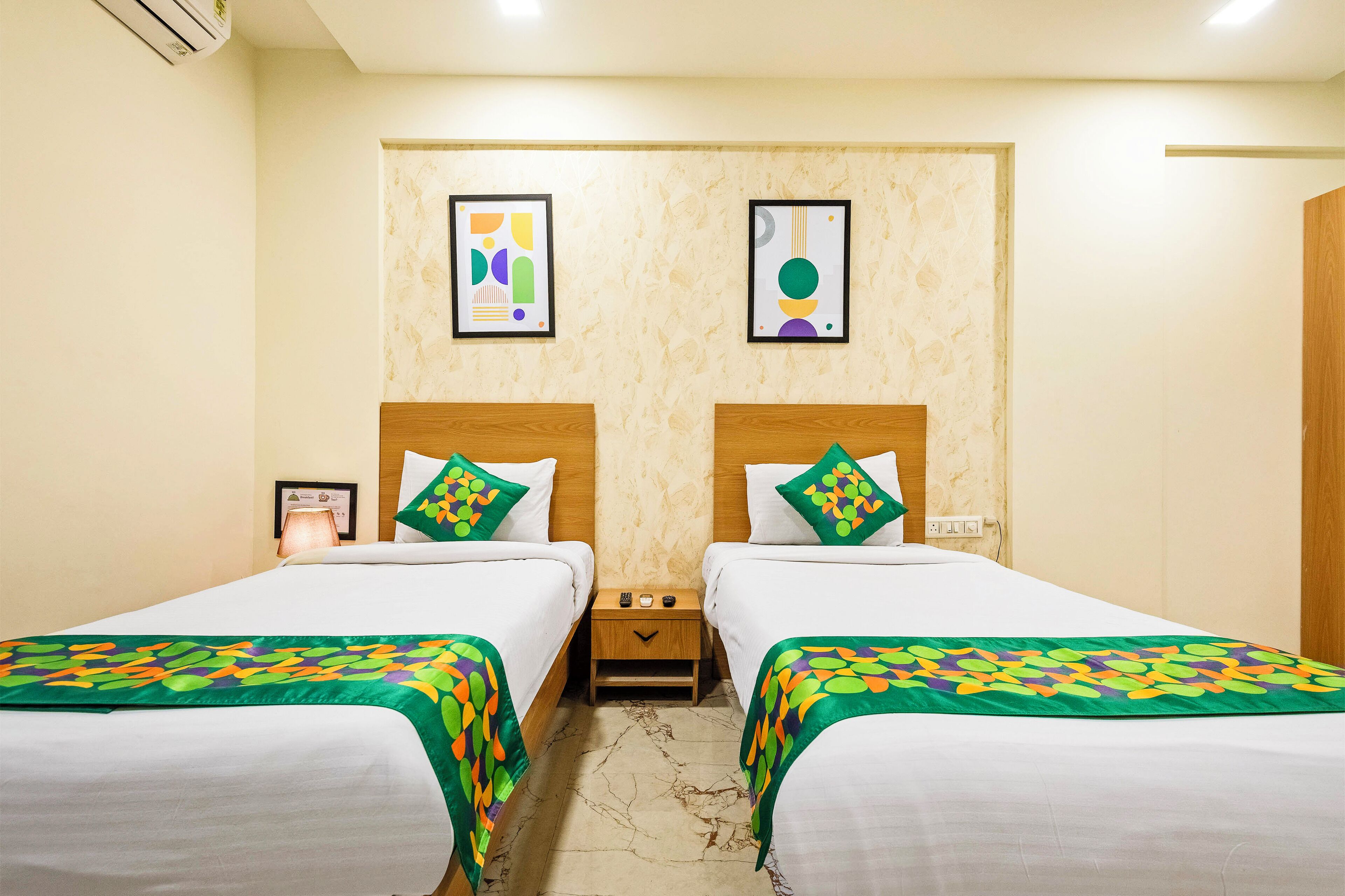 A hotel room with two beds, each with a green and white bedspread, a wooden headboard, and a nightstand with a lamp and a framed photo.