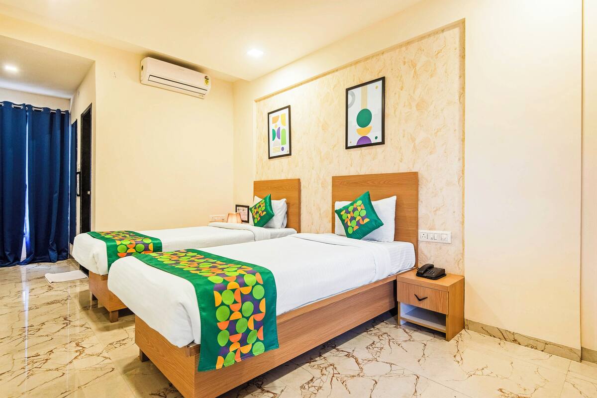 A hotel room with two beds, a nightstand, and a bathroom with a shower curtain.