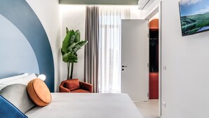 Una habitació d'hotel moderna amb un llit, una planta, una cadira i una televisió penjada a la paret.