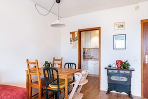 Un comedor con una mesa y sillas de madera, una pequeña cocina con un fregadero y armarios, y un aparador decorado con plantas.